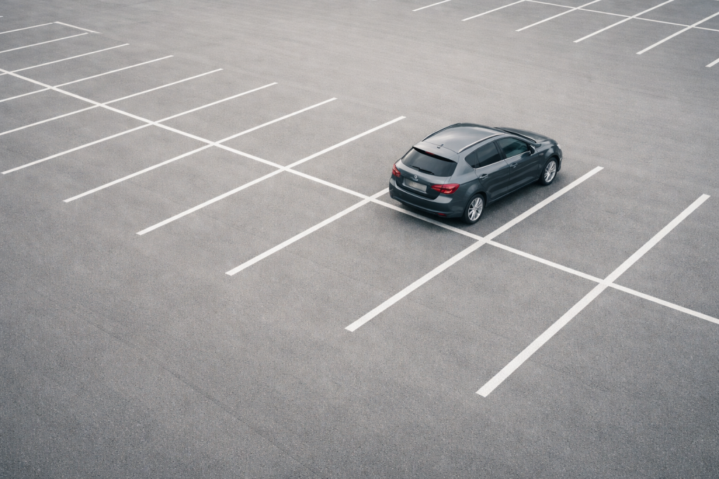 Standard blogheader: stemningsfuldt oversigtsbillede af en bil parkeret på en parkeringsplads eller ved vejkant, set oppefra/let skråt, med masser af negativ plads til overlay og bred anvendelse på tværs af emner.